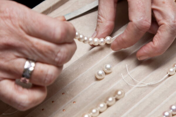 Close,Hand,Jeweler,Stringing,Pearls,On,A,Necklace